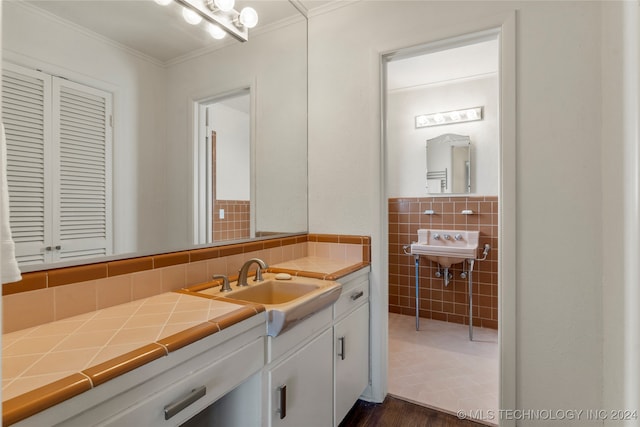 bathroom featuring tasteful backsplash, tile walls, wood-type flooring, ornamental molding, and sink