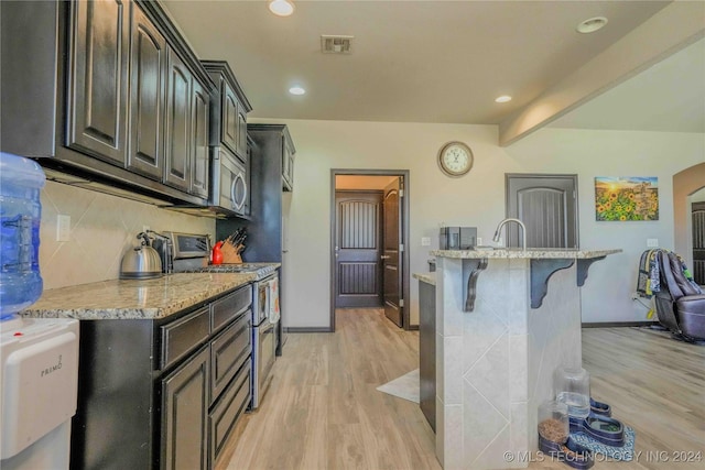 kitchen with light stone countertops, a kitchen bar, stainless steel appliances, tasteful backsplash, and light hardwood / wood-style flooring