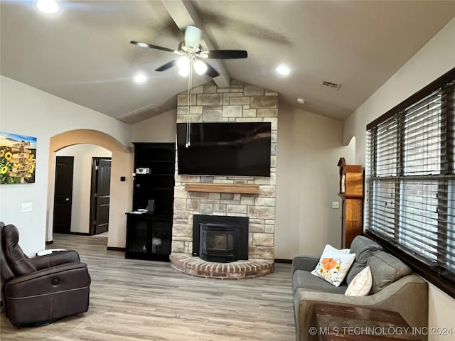 living room with ceiling fan, vaulted ceiling with beams, a wood stove, and light hardwood / wood-style floors