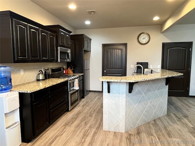 kitchen with appliances with stainless steel finishes, light hardwood / wood-style floors, a center island with sink, and a breakfast bar