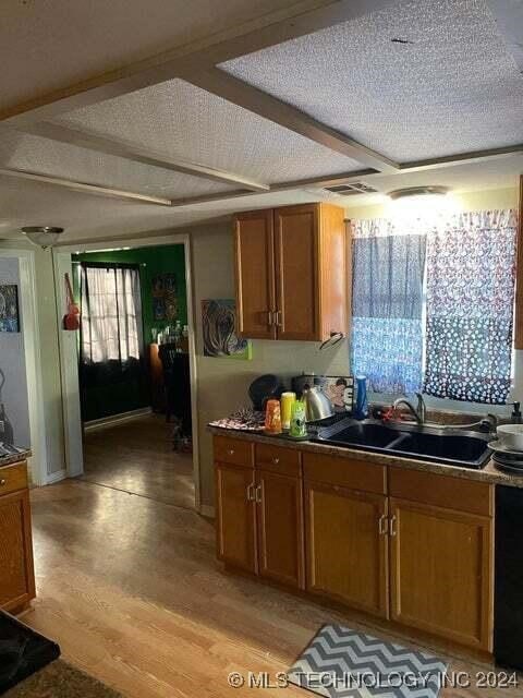 kitchen with sink, black dishwasher, light hardwood / wood-style floors, and a textured ceiling