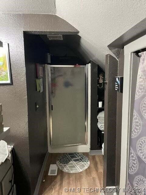 bathroom with wood-type flooring, a shower with door, vaulted ceiling, a textured ceiling, and vanity