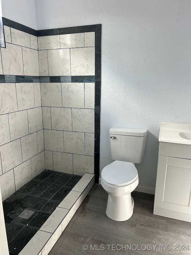 bathroom featuring hardwood / wood-style floors, vanity, toilet, and tiled shower