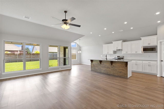 kitchen featuring backsplash, stainless steel appliances, light hardwood / wood-style flooring, white cabinets, and an island with sink