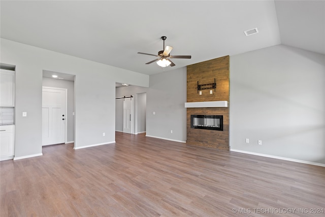 unfurnished living room with a barn door, ceiling fan, vaulted ceiling, and light wood-type flooring