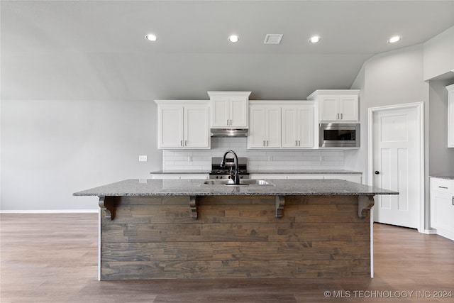 kitchen featuring sink, a center island with sink, stainless steel microwave, stone countertops, and dark hardwood / wood-style floors