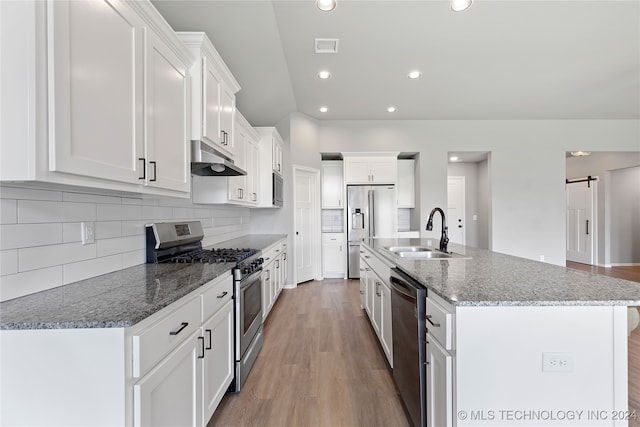 kitchen featuring white cabinets, sink, a barn door, a center island with sink, and appliances with stainless steel finishes