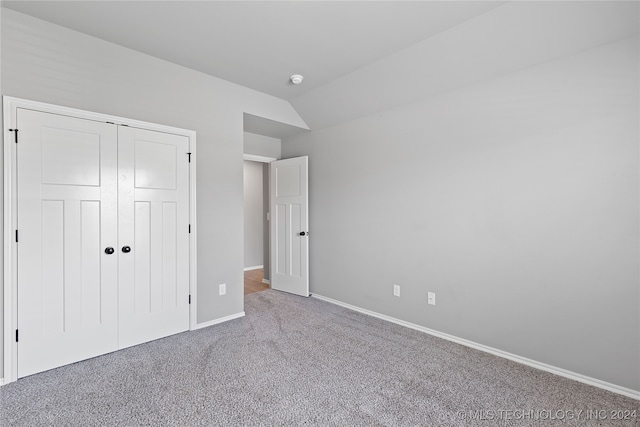 unfurnished bedroom with carpet, a closet, and lofted ceiling