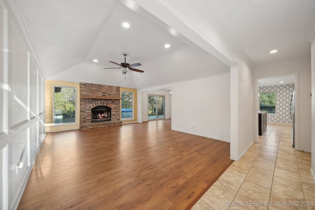 unfurnished living room with ceiling fan, a brick fireplace, crown molding, light hardwood / wood-style floors, and vaulted ceiling