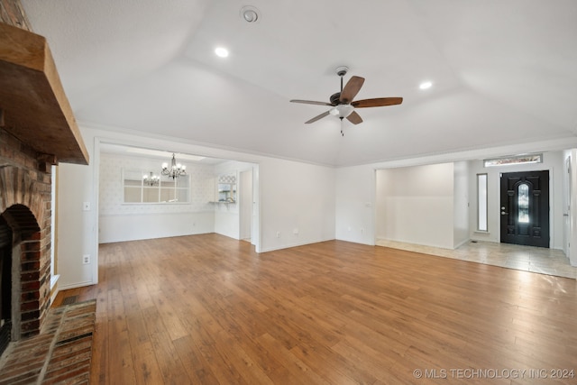 unfurnished living room with light hardwood / wood-style flooring, lofted ceiling, a fireplace, ceiling fan with notable chandelier, and ornamental molding