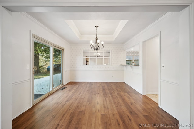 unfurnished dining area with a raised ceiling, hardwood / wood-style flooring, an inviting chandelier, and crown molding