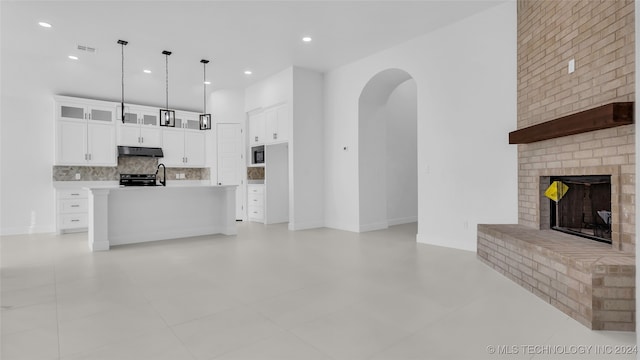 kitchen featuring pendant lighting, a kitchen island with sink, white cabinets, a brick fireplace, and tasteful backsplash