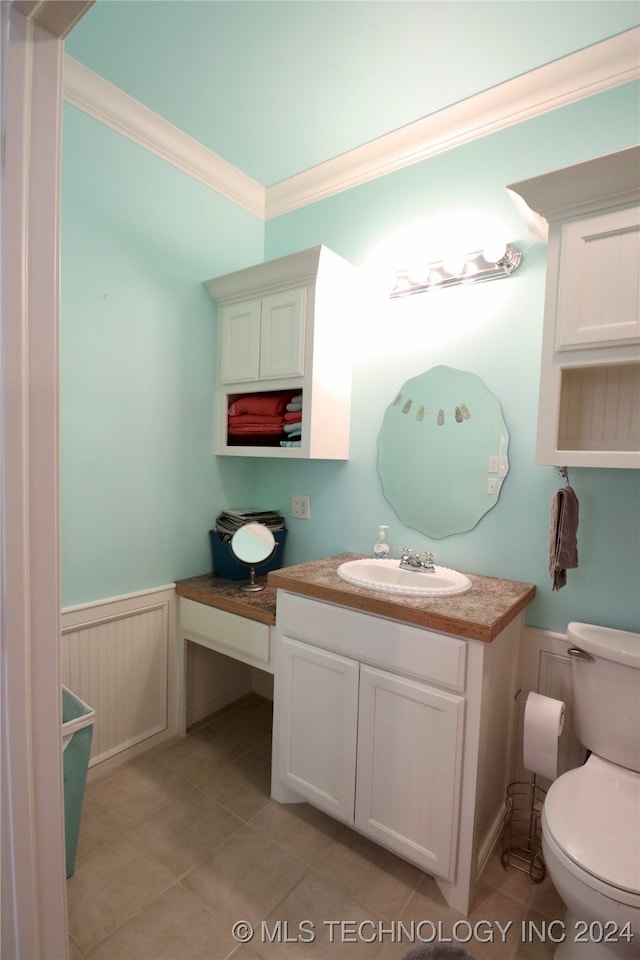 half bathroom with tile patterned floors, toilet, wainscoting, crown molding, and vanity