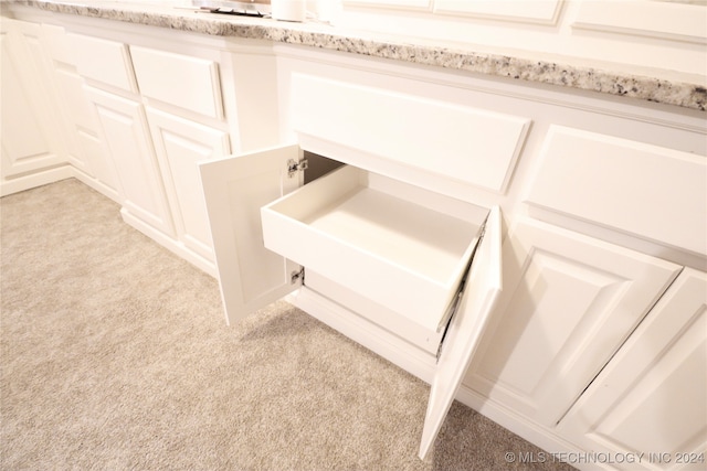 room details with white cabinets, light colored carpet, and light stone countertops