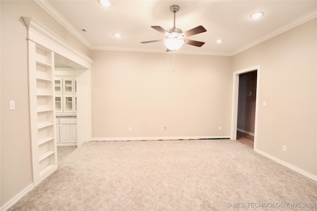 empty room with baseboards, light carpet, built in shelves, and crown molding