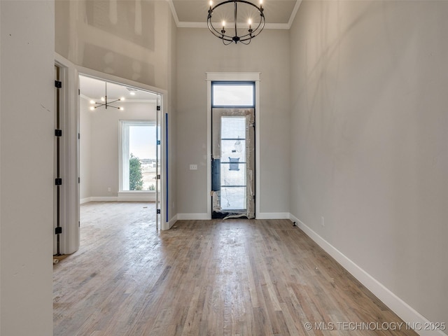 entrance foyer featuring a towering ceiling, ornamental molding, a chandelier, and light hardwood / wood-style flooring