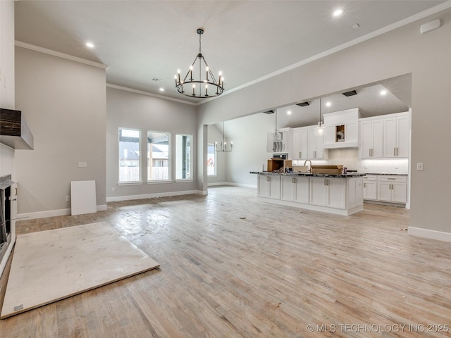 unfurnished living room featuring light wood-type flooring, a chandelier, crown molding, and sink