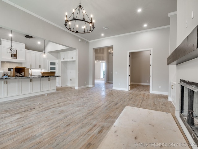 unfurnished living room with light hardwood / wood-style floors, sink, crown molding, and an inviting chandelier