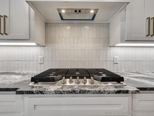 kitchen featuring stainless steel gas cooktop, decorative backsplash, white cabinets, and dark stone counters