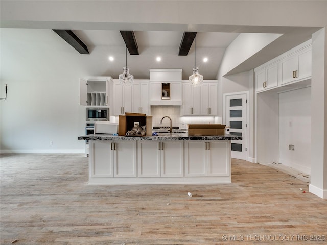 kitchen with dark stone countertops, hanging light fixtures, a kitchen island with sink, stainless steel appliances, and white cabinets