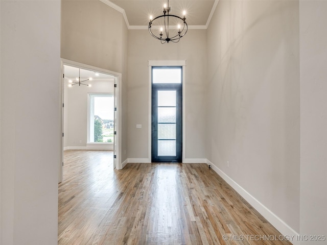 entryway with crown molding, a notable chandelier, wood finished floors, and a towering ceiling