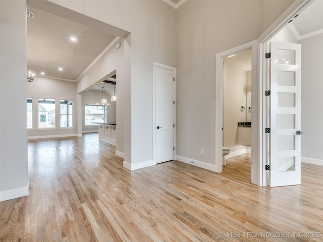 spare room featuring a notable chandelier, baseboards, ornamental molding, and light wood-style floors