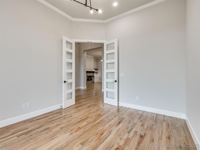 empty room with french doors, baseboards, ornamental molding, and light wood-style flooring