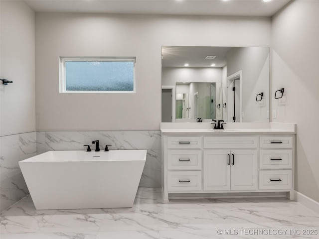 bathroom featuring recessed lighting, marble finish floor, vanity, wainscoting, and a freestanding tub