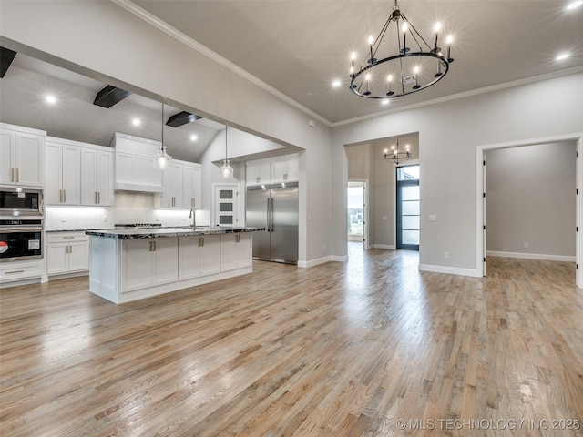 kitchen featuring open floor plan, an inviting chandelier, white cabinetry, built in appliances, and crown molding