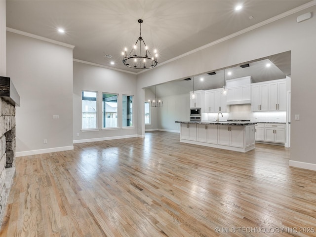 unfurnished living room featuring crown molding, a sink, a chandelier, light wood finished floors, and recessed lighting