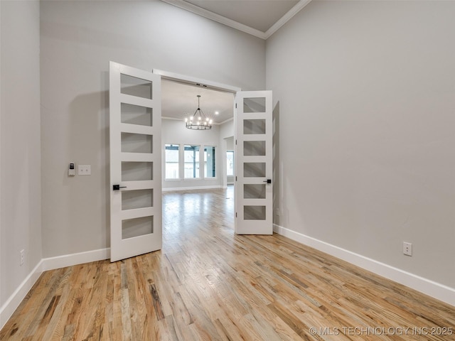 empty room with a notable chandelier, ornamental molding, french doors, and light wood-style floors