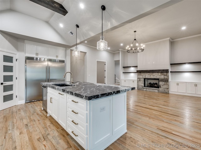 kitchen with stainless steel appliances, dark stone countertops, visible vents, a sink, and light wood-style flooring
