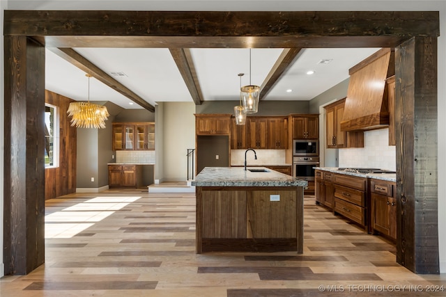 kitchen featuring beam ceiling, sink, a kitchen island with sink, appliances with stainless steel finishes, and light wood-type flooring