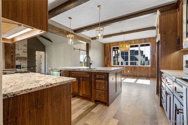 kitchen with sink, wood walls, an island with sink, light hardwood / wood-style floors, and decorative light fixtures