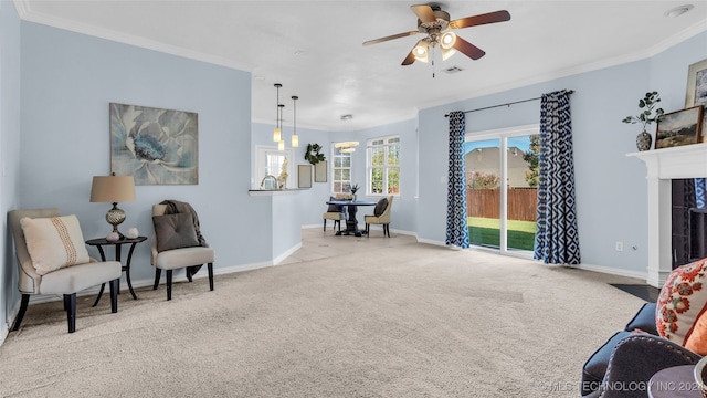 sitting room with a tiled fireplace, ceiling fan, light carpet, and ornamental molding