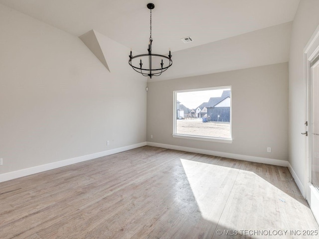 spare room with a chandelier and light wood-type flooring