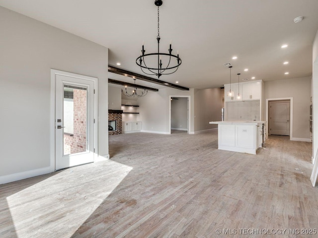 unfurnished living room featuring a chandelier, a brick fireplace, and light wood-type flooring