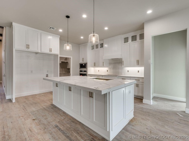 kitchen with premium range hood, white cabinetry, appliances with stainless steel finishes, a spacious island, and light stone countertops