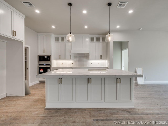 kitchen featuring a kitchen island with sink, light stone counters, white cabinetry, and appliances with stainless steel finishes