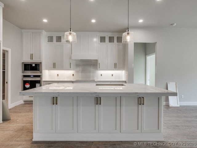 kitchen featuring built in microwave, white cabinetry, stainless steel oven, light stone countertops, and a spacious island