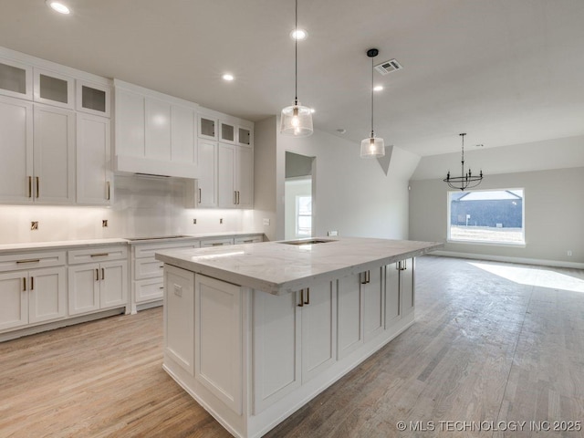 kitchen with a kitchen island, pendant lighting, white cabinets, light hardwood / wood-style floors, and light stone countertops