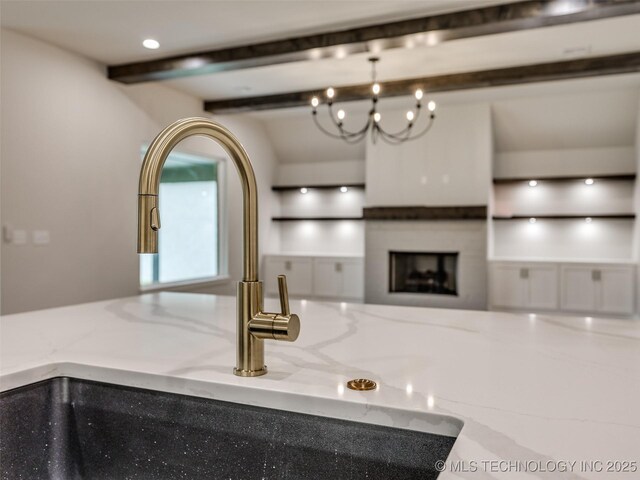 room details featuring light stone counters, a sink, beamed ceiling, and a fireplace