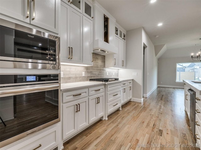 kitchen featuring white cabinets, stainless steel gas cooktop, built in microwave, light wood-style floors, and decorative backsplash