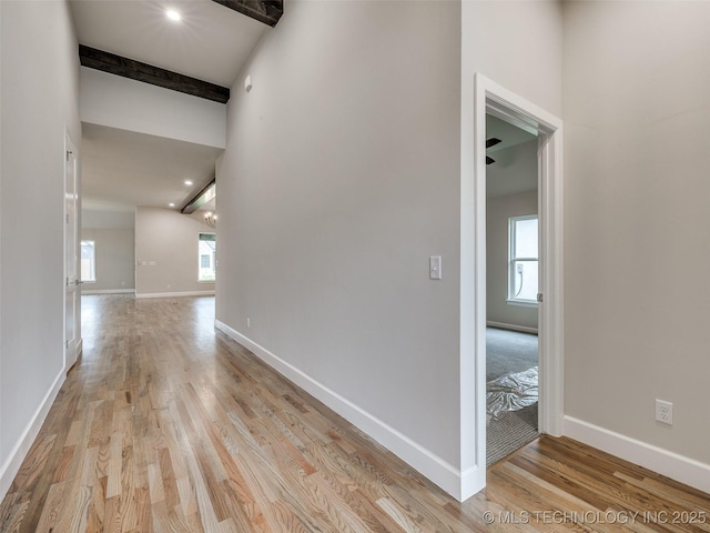 hallway featuring baseboards, beamed ceiling, and light wood finished floors