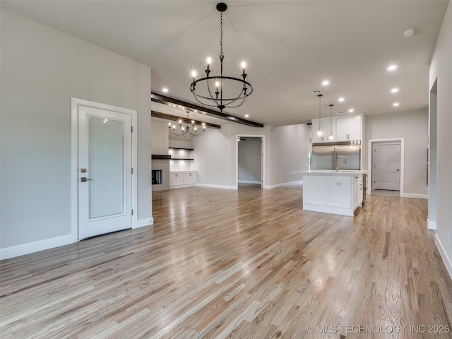 unfurnished living room featuring light wood finished floors, baseboards, recessed lighting, and a chandelier