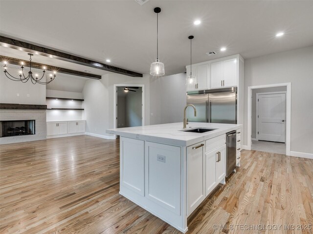kitchen featuring white cabinets, decorative light fixtures, stainless steel built in refrigerator, and a center island with sink