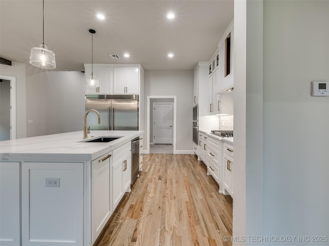 kitchen with built in appliances, white cabinetry, a sink, and light wood-type flooring
