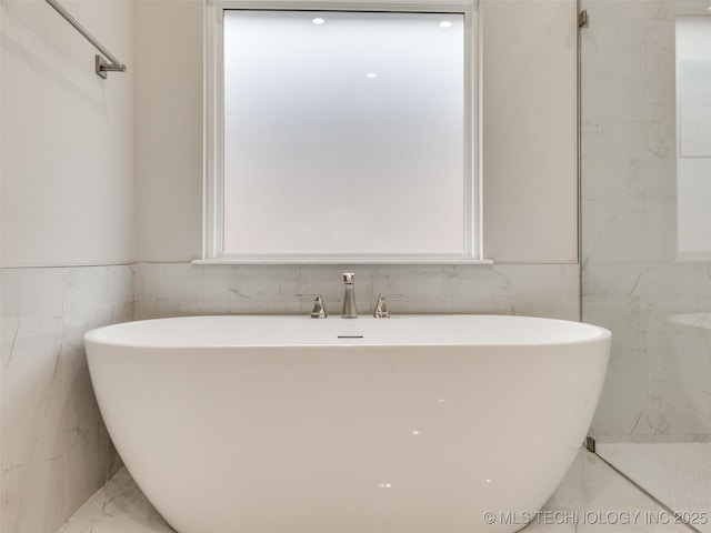 full bath with marble finish floor, a healthy amount of sunlight, a freestanding tub, and tile walls
