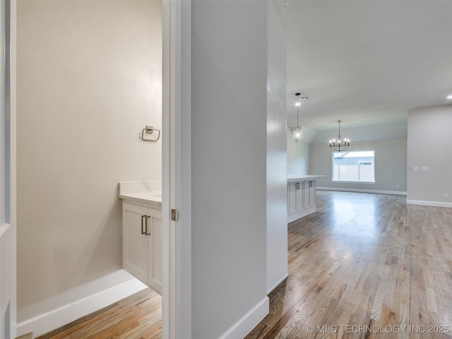 hall with light wood finished floors, baseboards, and an inviting chandelier