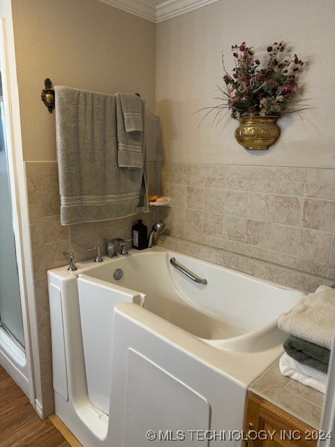 bathroom with a tub to relax in, hardwood / wood-style flooring, and ornamental molding